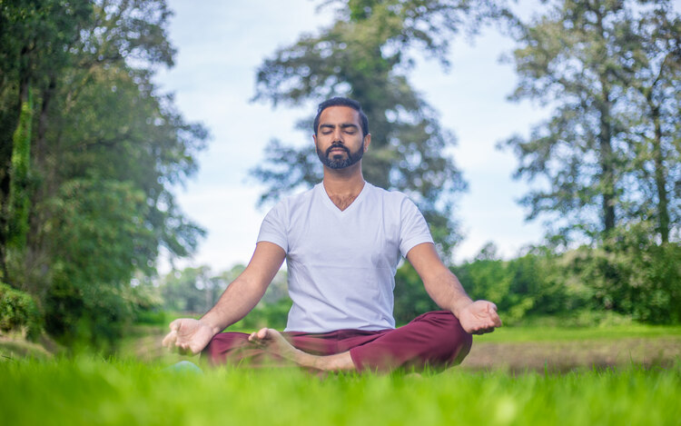 A yoga teacher sits in lotus pose outside in nature, practicing Kapalbhati Pranayama for metabolism increase 