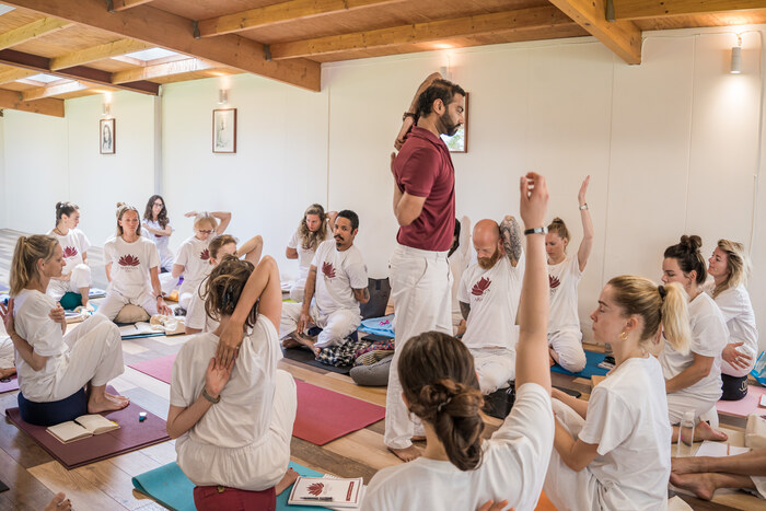 Yoga teacher demonstrating shoulder-opening pose to students during a 200-hour yoga teacher training at an ashram