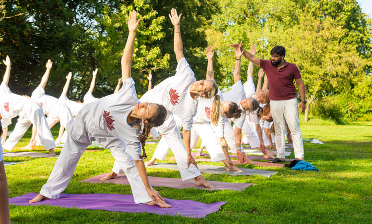 Students practising Triangle Pose outdoors with an instructor during Hatha yoga teacher training